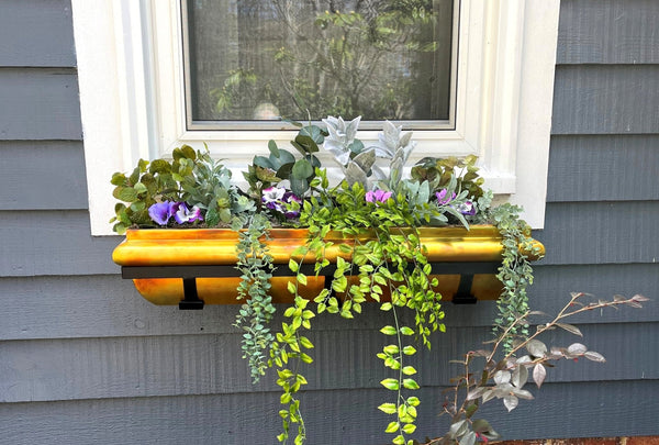 H Potter brand copper window boxes with flowers hanging on the outside of a house above a flower garden with planters